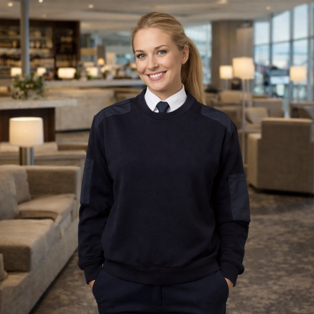 Woman in a navy uniform standing in a modern hotel lobby.